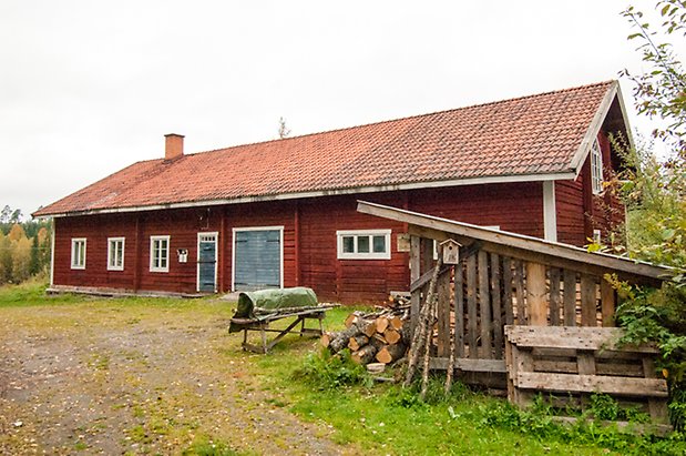 Lits Prästbord 1:18. Röd, timrad ladugård med en blå dubbelport och en blå port, fönster med vita spröjs.