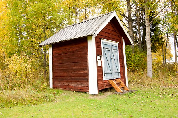 Lits Prästbord 1:18. Liten byggnad i röd panel med blå dubbelport.