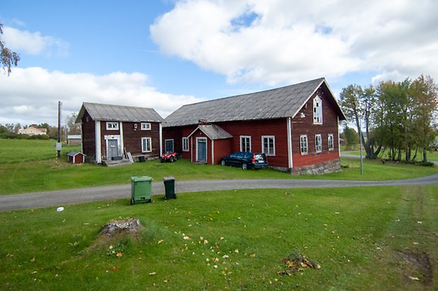 Prisgård 1:24. Ladugård i två våningar i röd panel med blå dubbelport och fönster med vita spröjs. Hus i två våningar byggt i vinkel med blå dubbeldörr och fönster med vita spröjs.