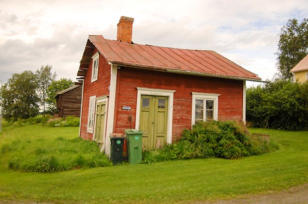 Bräcke 2:5. Litet hus i två våningar i röd panel med två gröna dubbeldörrar och fönster med vita spröjs. Huset lutar.