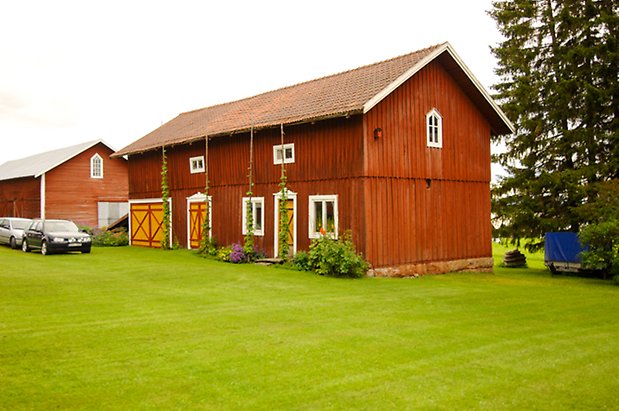 Digernäs 2:7. Byggnad i två våningar i röd panel med fönster med vita spröjs, två dubbelportar och en dörr i gult och rött.