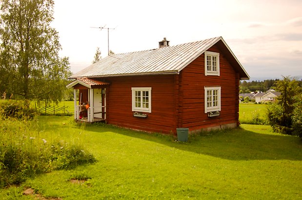 Fannbyn 1:6. Timrat, rött hus i två våningar med förstukvist och fönster med vita spröjs.