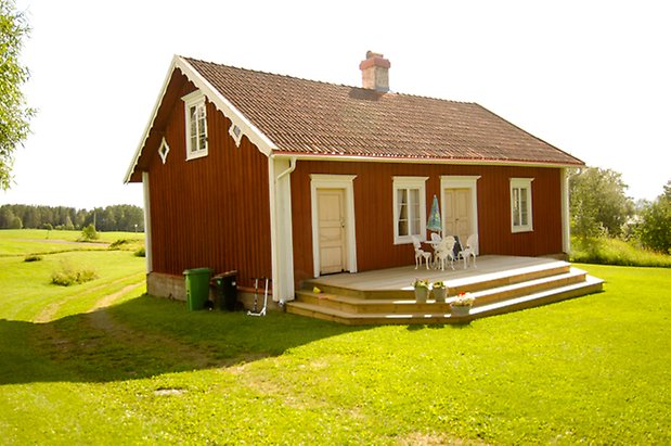 Måläng 2:29. Hus i två våningar i röd panel med trädäck framför, med fönster med vita spröjs och en gul dörr och en gul dubbeldörr.