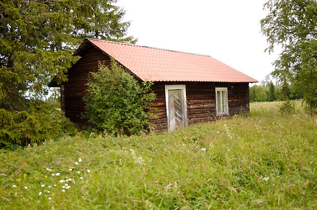 Slandrom 2:14. Brun, timrad byggnad med grå dörr och fönster med vita spröjs.