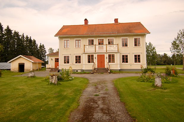 Sunne Prästbord 1:13. Hus i två våningar i ljus, liggande panel med röd dubbeldörr, och fönster med röda spröjs.