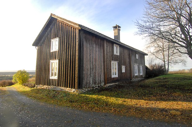 Bjärme 8:23. Byggnad i två våningar i grå panel med fönster med vita spröjs, skorsten på taket.