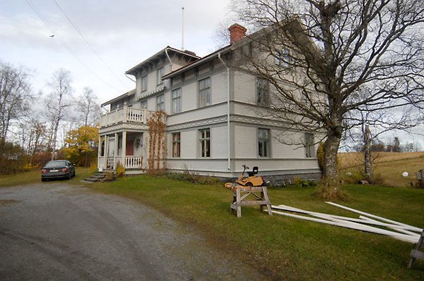 Månsta 1:13. Villa i tre våningar i ljusgrå, liggnade panel med grå detaljer, förstukvist med balkong ovanför.