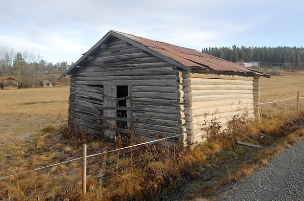 Åsan 1:2. Grå, timrad byggnad.