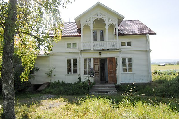 Norderöns-Backen 1:12. Villa i vit liggande panel i två våningar, punschveranda med balkong ovanför med snickarglädje, fönster med vita spröjs.