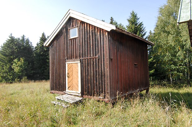 Norderöns-Backen 1:12. Byggnad i brun panel i två veckor, med gul port med ett litet fönster ovanför.