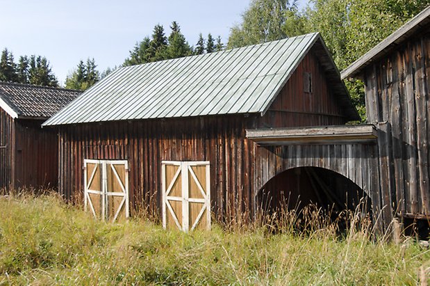 Norderöns-Backen 1:12. Byggnad i brun panel med två gul/vita dubbelportar bredvid byggnad med grå panel med en halvcirkelformad öppning,