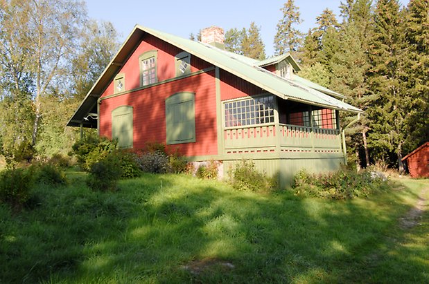 Trusta 2:5. Villa i röd, liggande panel med gröna detaljer, veranda i grönt med snickarglädje, fönsterluckor i grönt och fönster med gröna spröjs.