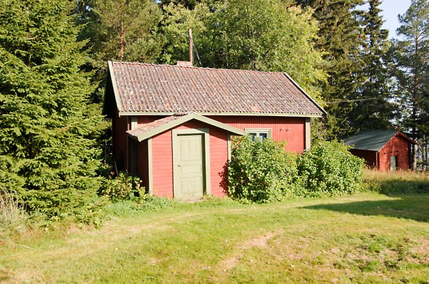 Trusta 2:5. Stuga i röd liggande panel med gröna detaljer och grön dörr.