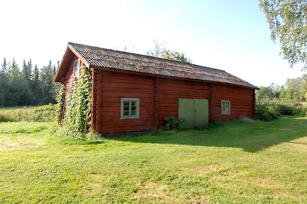 Trusta 2:5. Byggnad i rött timmer med grön dubbelport med fönster med gröna spröjs, slingerväxter på kortsidan.