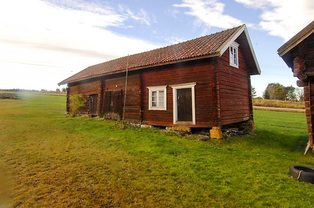 Öd 2:2. Röd/brun byggnad i timmer, fönster med vita spröjs, svart dörr, en svart dubbelport och en svart port.