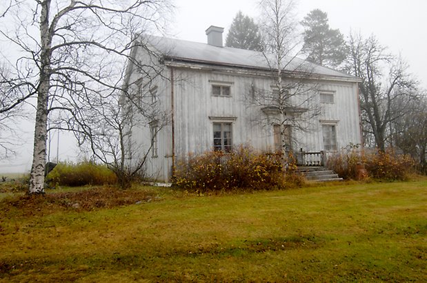 Kläppe 1:1. Villa i två våningar i vit panel med liten trapp upp till en brun dubbeldörr, fönster med vita spröjs och grå skorsten.