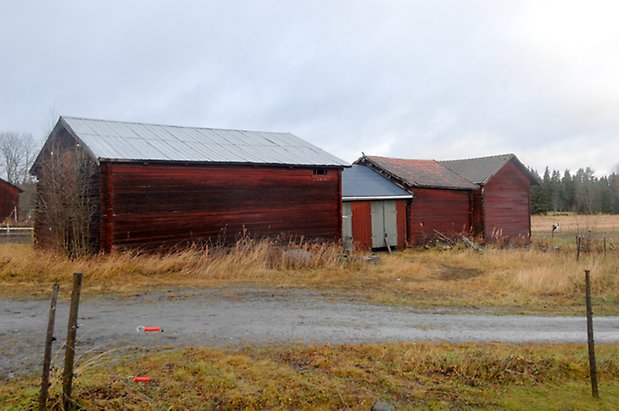 Brynje 1:29. Bygnagd i rött timmer bredvid en mindre byggnad i röd panel med två gröna dubbelportar, bredvid två röda, timrade byggnader.