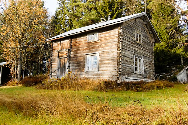 Österåsen 5:5. Hus i grått timmer i två våningar, brun dubbeldörr och fönster med spröjs.