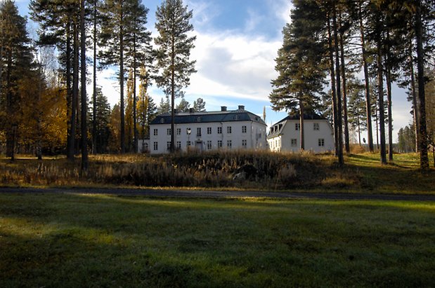 Österåsen 9:26. Byggnader i vit puts i tre våningar med svart tak.