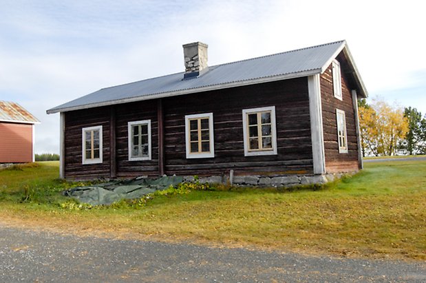 Österåsen 10:7. Hus i brunt timmer med vita detaljer, fönster med gula spröjs, murad skorsten.