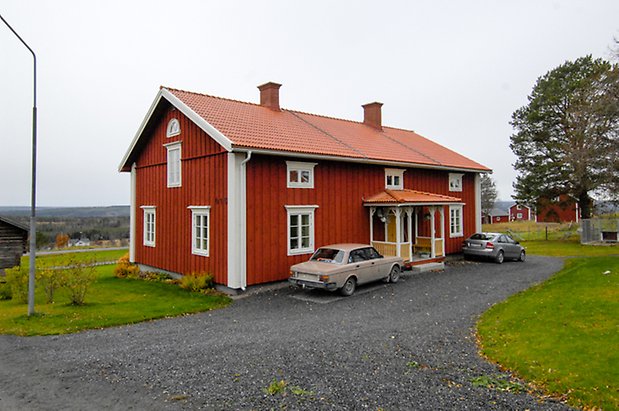 Backegård 1:23. Hus i två våningar i röd panel med vita detaljer, fönster med vita spröjs, förstukvist i vitt och gult, gul dubbeldörr, två skorstenar.