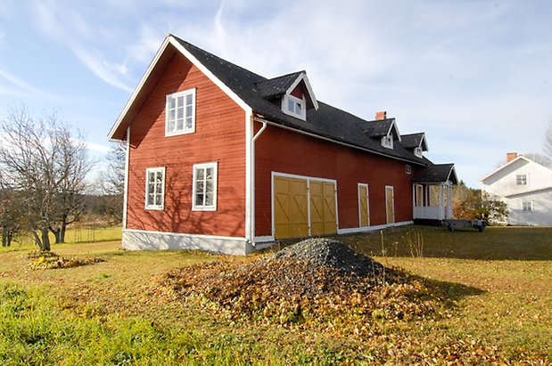 Storhögen 4:25. Byggnad i rött timmer med vita detaljer i två våningar, fönster med vita spröjs, gula portar, förstukvist i rött och vitt med snickarglädje.