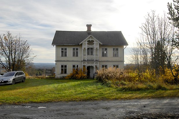 Storhögen 6:8. Villa i ljusgul panel med vita detaljer, fönster med vita spröjs, förstukvist med balkong ovanför med snickarglädje.