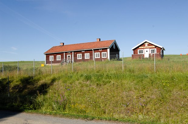 Kungsgården 5:4.  Hus i röd panel med vita detaljer, fönster med vita spröjs, brun dörr. Bredvid en röd, timrad byggnad med vit dörr.