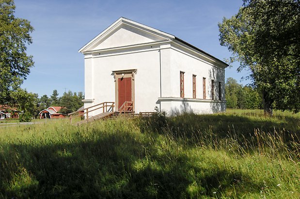 Stocke 2:2. Byggnad i vit puts, röd dubbeldörr, fönster med röda spröjs.