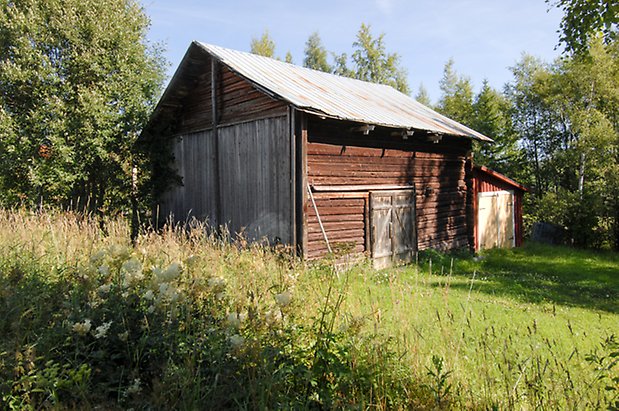 Vagle 4:10. Timrad, grå lada med dubbelport, tillbyggnad i röd panel med gul dubbelport och snedtak.