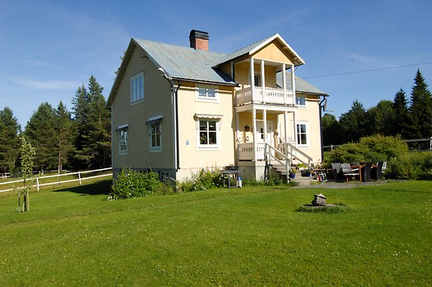 Västbyn1:2. Villa i ljusgul liggande panel med vita detaljer i två våningar, fönster med vita spröjs, förstukvist med balkong ovanför.