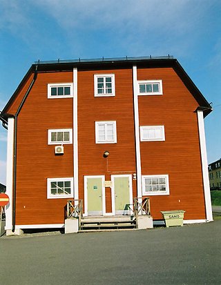 Fältjägaren 6. Stort rött hus i tre våningar med svart tak och vita fönster med spröjs, sett från sidan.