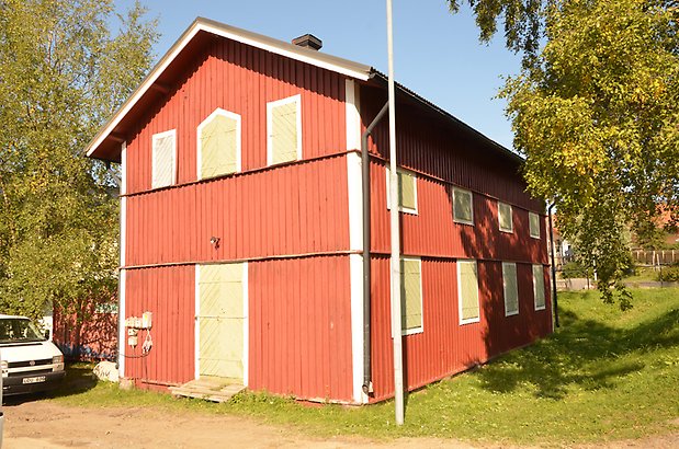 Lugnet 7, hus 50 - Gammal röd förrådsbyggnad i två våningar med gröna dörrar och gröna fönsterluckor.