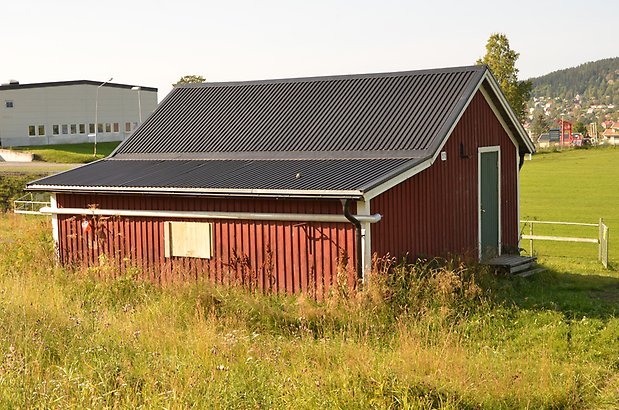 Norr 1:4. litet rött trä hus med grön dörr och fönsterlucka.