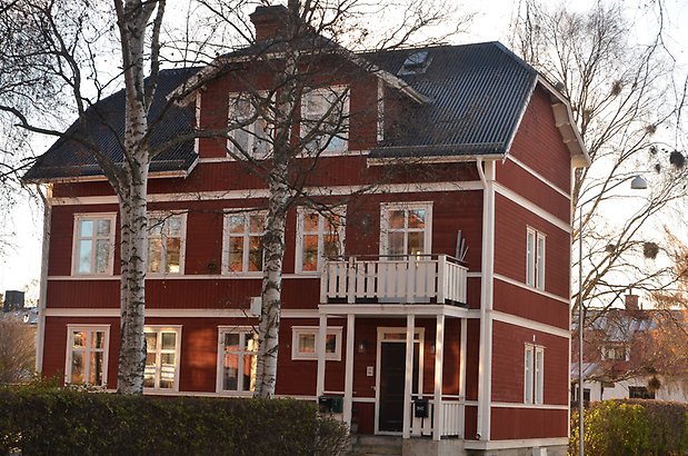 Nässlan 3. Villa i röd, liggande panel och vita fönster med spröjs, vit förstukvist med balkong.