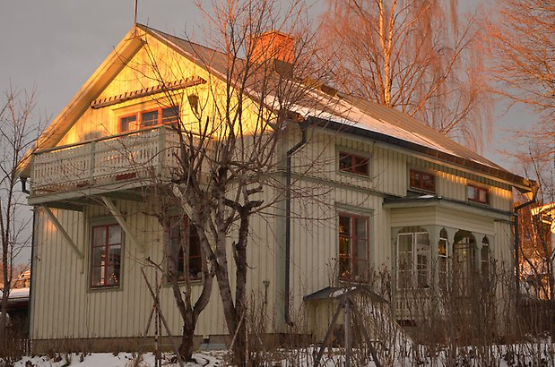 Svärtan 7. Villa i ljusgrön träpanel och gröna detaljer, balkong och förstukvist med snickarglädje.