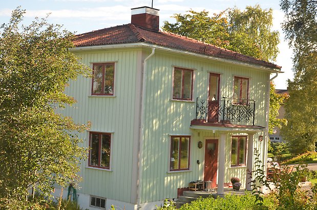 Bergsvik 1. Villa i ljusgrön panel men rosa detaljer, röda fönster och balkong i smide.