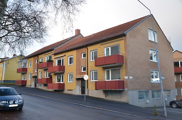 Byggmästaren 7. Bostadshus i brun och gul puts med röda balkonger och vita fönster.