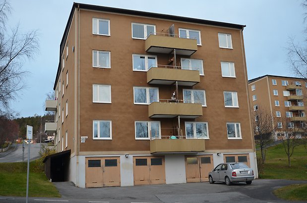 Fiolen 1. Bostadshus i fem våningar i brun puts, vita fönster, beige balkonger och beige garageportar.