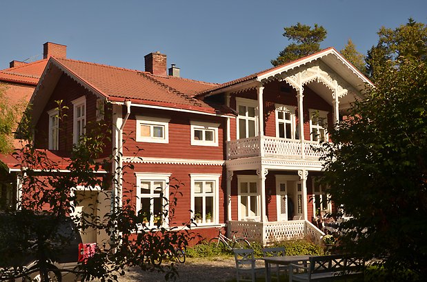 Fritzhem 14. Villa i röd, liggande panel, vita fönster med spröjs och förstukvist med balkong med vit snickarglädje.