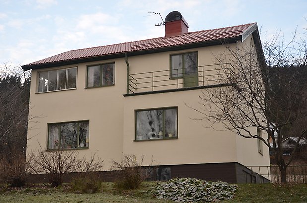 Lantbrukaren 4. Villa i beige puts med svarta fönster och balkong.