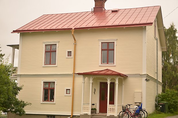 Muraren 3 a. Villa i ljusgul, liggande panel med röda fönster och förstukvist, rött plåttak.