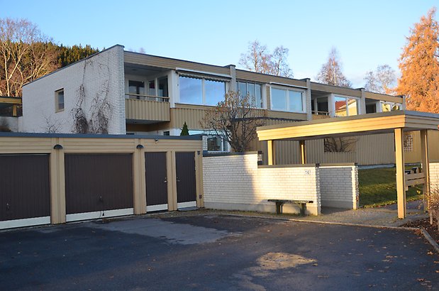 Östbergsgården 2-18. Bostadshus i två våningar i gul panel och vitt tegel, garagelänga i gul panel med bruna garageportar.