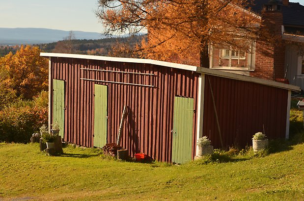 Berghem 10. Byggnad i brun träpanel och gröna dörrar, sluttande tak.