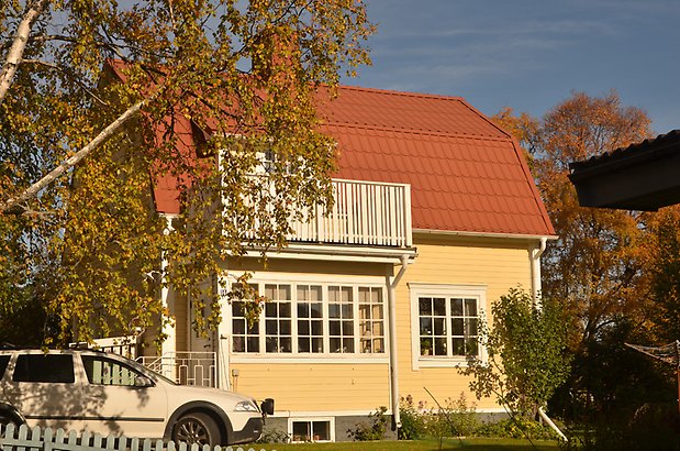 Hyvlaren 12. Villa i gul, liggande panel med vita fönster med spröjs och balkong. 