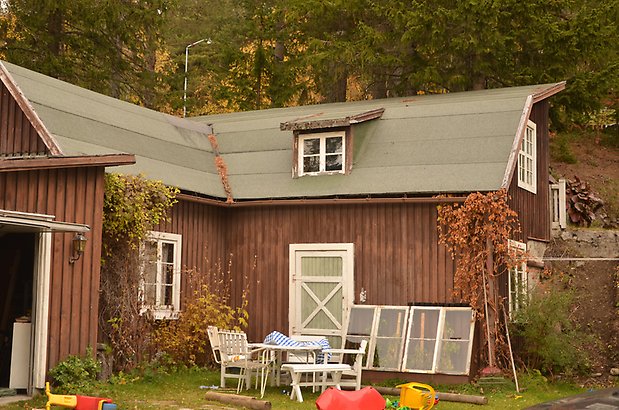 Tullvaktmästaren 1 b. Byggnad i brun panel med vita fönster med spröjs och grön dörr med ett kryss. 