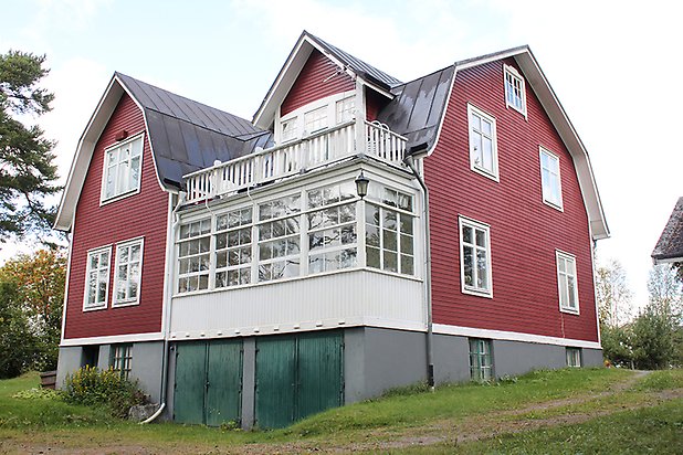 Brunflo-Viken 1:23. Villa i röd liggande panel, veranda med mycket fönster, vita fönster med spröjs och gröna garageportar.