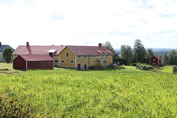 Kogsta 1:31. Byggnad i gul, liggande panel med vita fönster med spröjs, bruna dörrar och garageportar och rött plåttak.