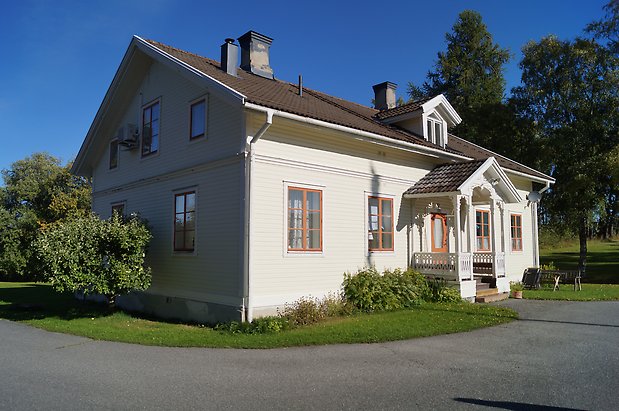 Ope 5:39. Villa i två våningar, ljusgul panel med vita detaljer, fönster med röda spröjs, röd dörr, förstukvist med snickarglädje.