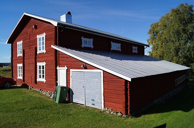 Torvalla 3:33. Röd, timrad byggnad i två våningar med fönster med vita spröjs, tillbyggnad med sned tak och blå dubbelport.